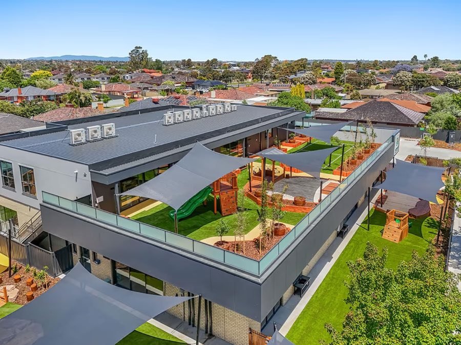 Aerial view of a two-storey childcare centre with a rooftop play deck and shade sails